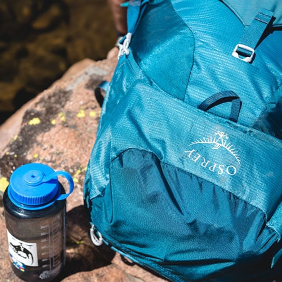 a Nalgene waterbottle sits next to an Osprey backpacking pack on a rock