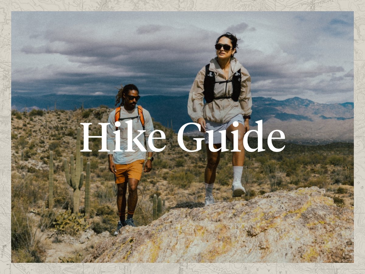 Two people hike in the desert as a storm brews in the distance.