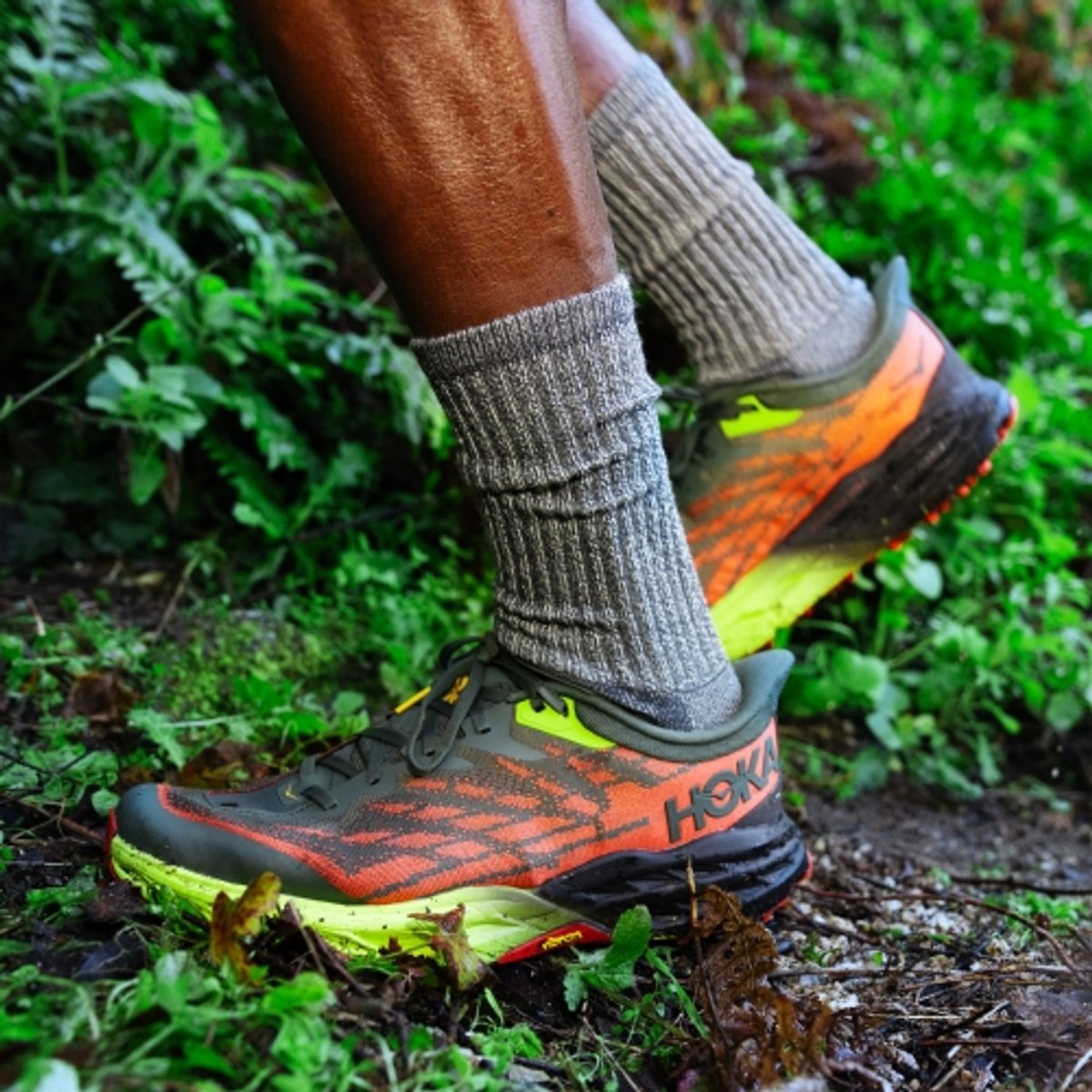 A detail shot of a hiker's shoes as he makes a stride on a trail with lush vegetation. 