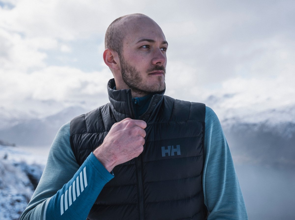 A man zips up a puffy vest in the snowy mountains.