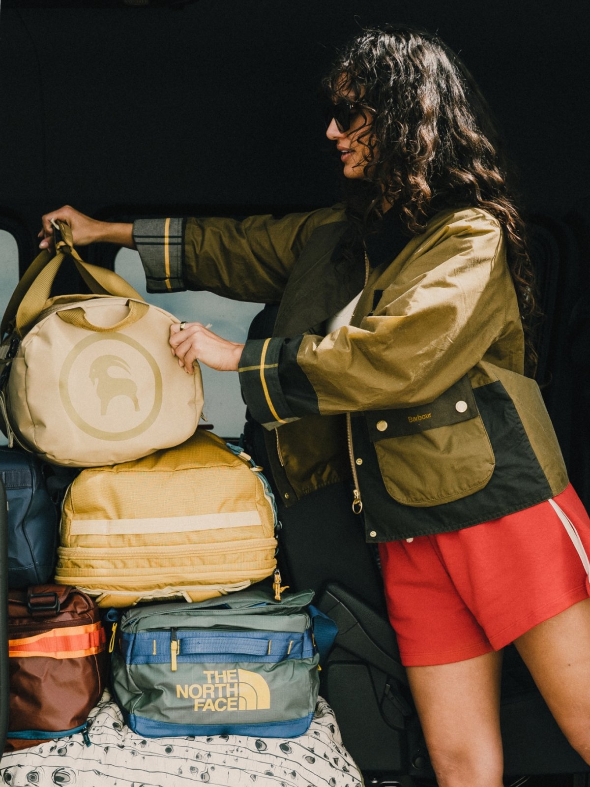 A woman adds a Backcountry 澳洲幸运5开奖官网开奖 Duffel Bag onto a pile of other large travel bags.
