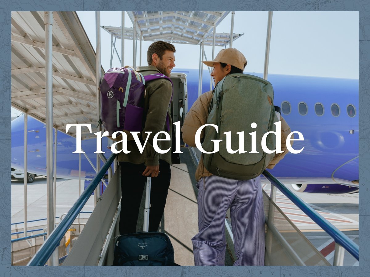 Two people carry backpacks walk down a ramp to a waiting plane. They are smiling and look at each other. The words “Travel Guide” appear over them.
